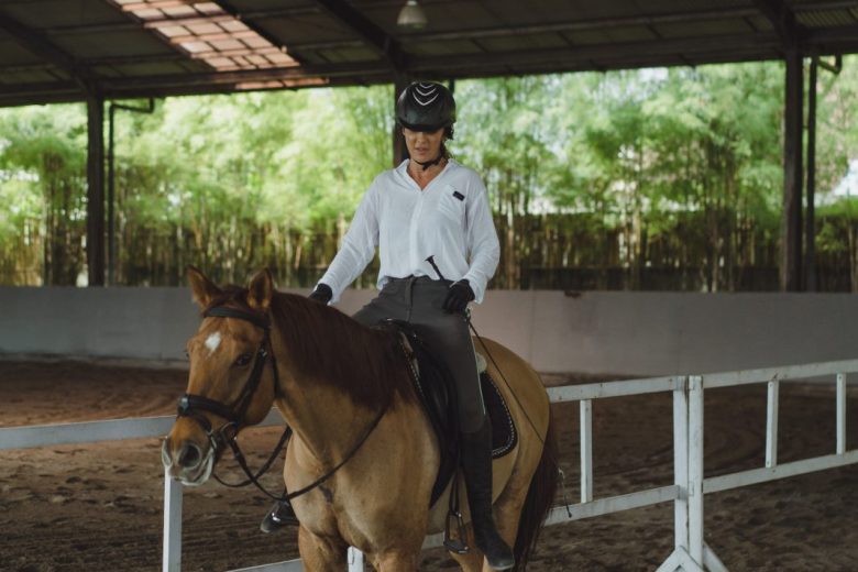 Young woman trains in horseback riding in the arena. Young Caucasian woman in formal clothing horseback riding across the sandy arena. A pedigree horse for equestrian sport. The sportswoman on a horse. The horsewoman on a horse. Equestrianism. Horse ridin
